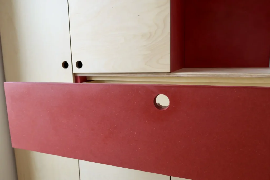tiroir ouvert en valchromat rouge d'un dressing fabriqué sur mesure pour une chambre d'enfant. La conception en bois contreplaqué bouleua et valchromat rouge est très contemporaine.